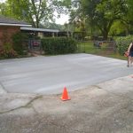 A freshly laid concrete area with traffic cones, featuring a person assessing the surface near a residential property.