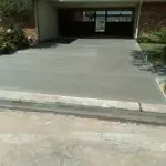 A freshly completed concrete driveway beside a home, featuring a smooth surface and surrounded by landscaping.