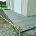Freshly poured concrete slab with caution tape surrounding the area, ready for use beside a metal building.