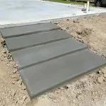 Freshly poured concrete steps leading up to a foundation, surrounded by loose soil and gravel.