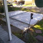 A partially completed outdoor foundation framed with wooden boards and covered by a tarp, surrounded by grass and pathways.