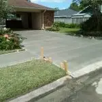 A freshly poured concrete driveway with wooden forms in a residential setting surrounded by landscaping and flowers.